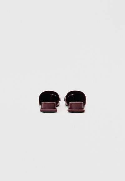 Burgundy leather slide sandals with open toes, flat soles, and minimalistic design; smooth texture with no visible patterns or hardware.