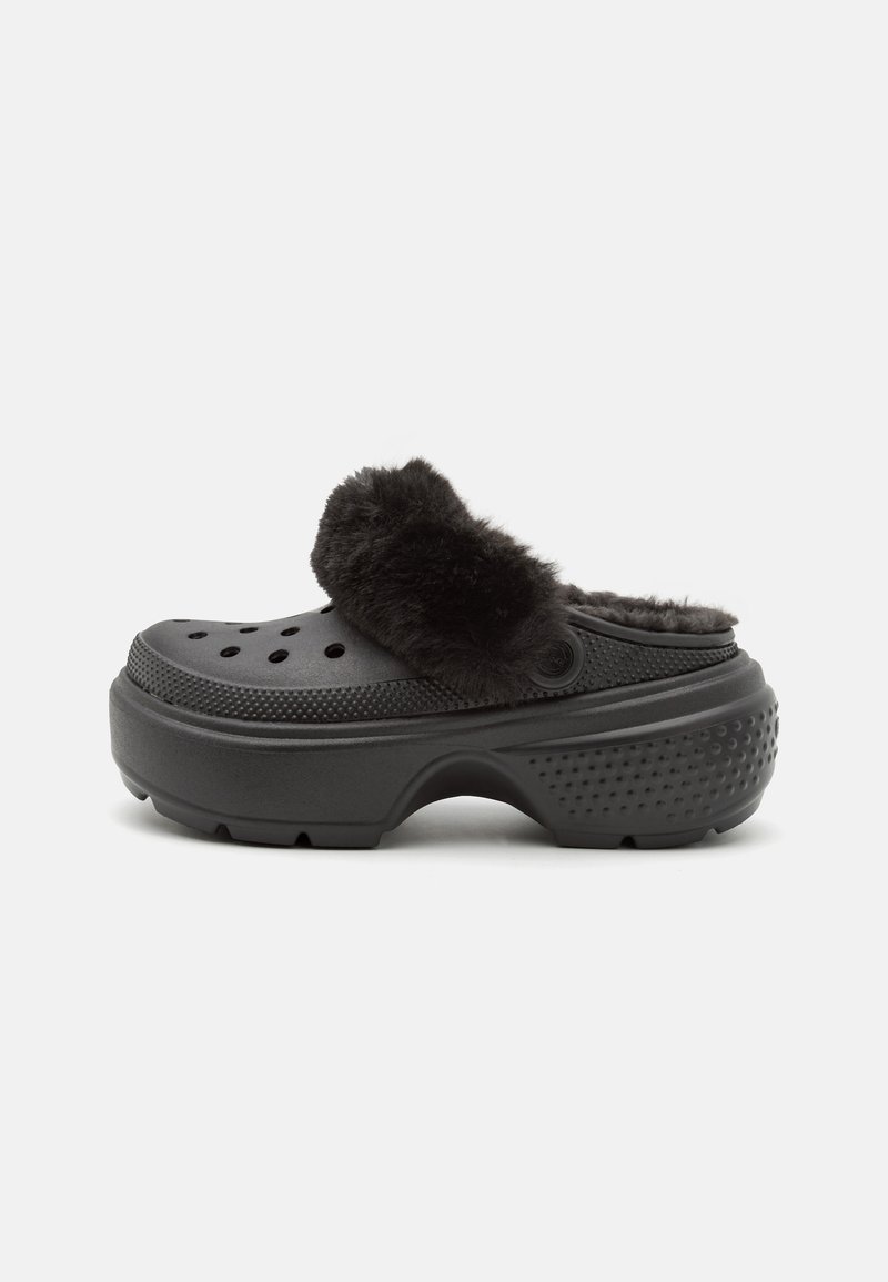 Black clogs with a soft, fuzzy upper band, featuring perforations on the front and a textured heel for grip. Lightweight and slip-on design.