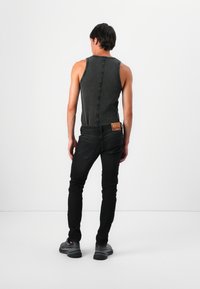 Camiseta de tirantes negra con costuras en contraste, combinada con jeans de mezclilla negros ajustados. Un detalle notable es una etiqueta de marca de color en la cintura.
