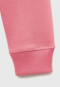 Detailní záběr na růžovou mikinu se zaměřením na texturu látky a žebrovaný manžetový detail na světlém pozadí.