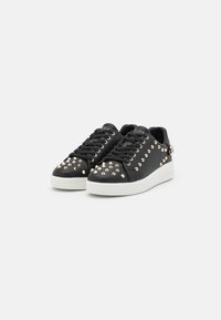 Sneaker nere in pelle con borchie in metallo dorato, suola bianca piatta, punta rotonda e lacci neri, con logo sulla linguetta e sul lato.