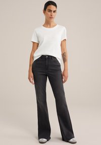 Witte katoenen t-shirt en hoogzittende zwarte flared jeans. De jeans hebben een gladde textuur en een lichte vervaging. Accentuatie met een metalen knoop.