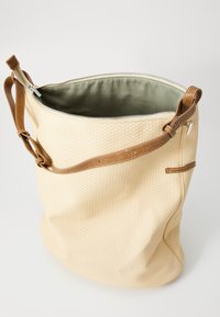 Beige woven tote bag with a textured surface, brown leather strap, and zip closure; features an olive green lining inside.