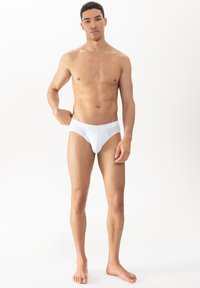 Weiße Baumwollslips mit glatter Textur, ausgestattet mit einem breiten elastischen Bund und einem klassischen Schnitt. Getragen von einem stehenden männlichen Modell.
