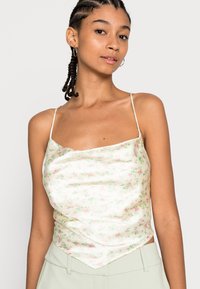 Top floral sedoso com fundo creme decorado com pequenas flores rosas e verdes, alças finas e uma bainha em forma de triângulo.