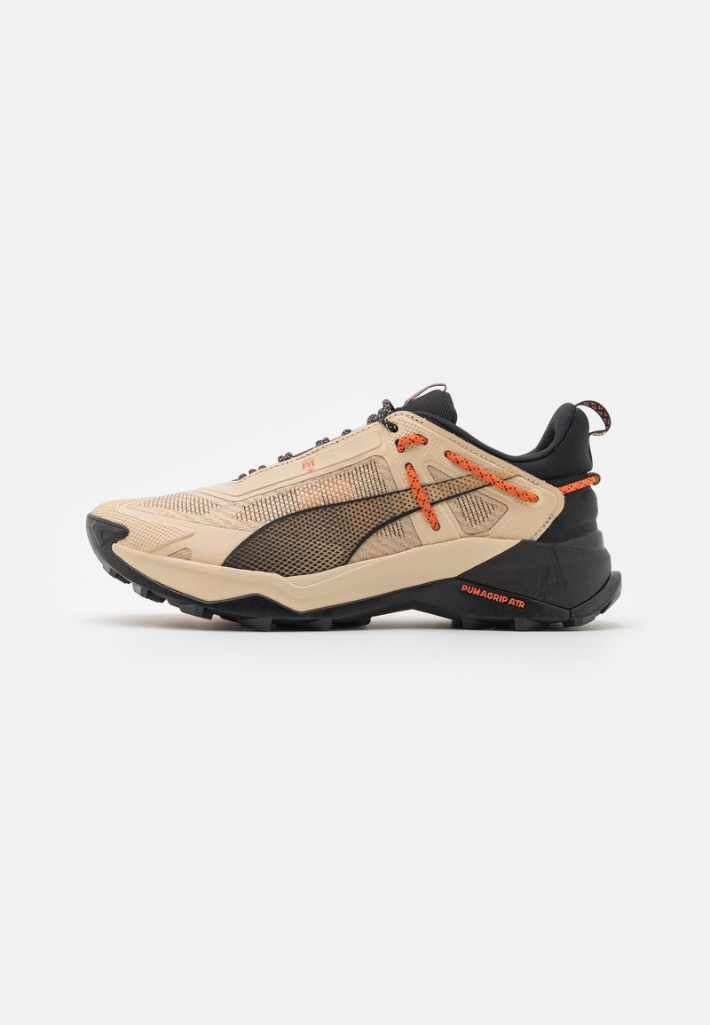 Chaussure de sport beige et noire avec des lacets et accents orange, panneau latéral en mesh, semelle épaisse noire avec l'étiquette "PUMAGRIP ATR."