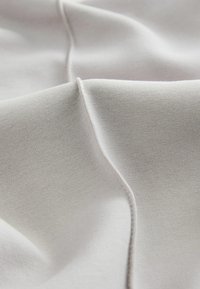 Light gray fabric with a smooth texture, featuring subtle stretch and curved creases. Stitched seams are visible along the edges.