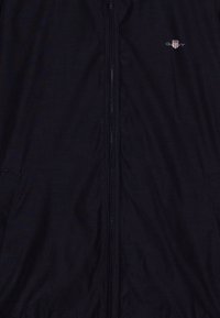 Giacca zip-up blu navy realizzata in tessuto leggero, con tasche laterali, una texture sottile e un piccolo logo sulla parte superiore del lato sinistro del petto.