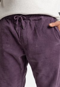 Lilla corduroy bukser med elastisk liv, snøring og sidelommer; har en myk tekstur og subtil ribbet mønster.