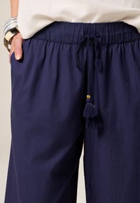 Marineblauwe, lichtgewicht broek met een elastische tailleband, trekkoord en decoratieve kwast. Beschikt over zijzakken en een relaxte pasvorm.