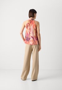 Halterneck-Top aus leichtem, mehrfarbigem Stoff mit einer Mischung aus Rosa- und Orangetönen; kombiniert mit lockeren beigen Hosen.