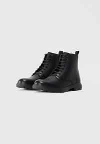 Botas de tobillo de cuero negro con un acabado suave, punta redonda, diseño con cordones, suelas de goma y lengüetas en la parte trasera para facilitar su uso.