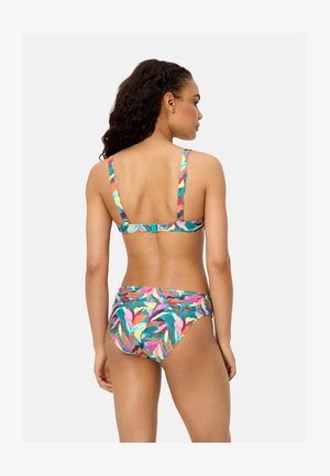 Mujer vistiendo un bikini con estampado tropical colorido, de espaldas, mostrando las tiras ajustables y el cierre de broche en la parte trasera del top del bikini.