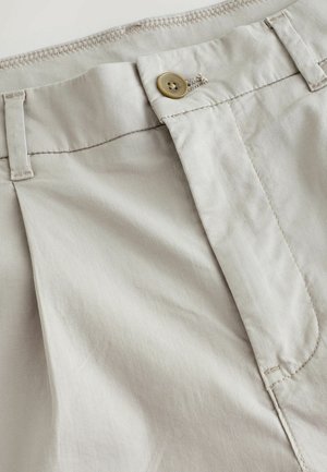 Pantalons beiges en tissu léger, avec une fermeture éclair, un bouton en laiton et des détails de couture subtils le long de la taille.