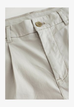 Pantalons beiges en tissu léger, avec une fermeture éclair, un bouton en laiton et des détails de couture subtils le long de la taille.