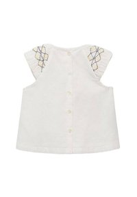 Top bianco in cotone con maniche corte a volant. Presenta decorazioni a forma di diamante ricamate sulle maniche e una chiusura con bottone sul retro.