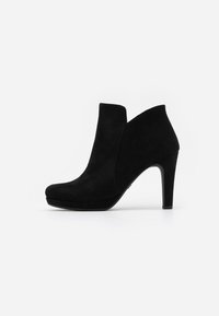Černá semišová kotníková bota s zakřiveným designem, vysokým stiletto podpatkem a kulatou špičkou, s výřezovými detaily na svršku.