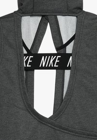 Tummanharmaa urheilullinen toppi, jossa syvä V-pääntie, musta merkitty nauha takana ja kontrastiväriset verkkoyksityiskohdat.