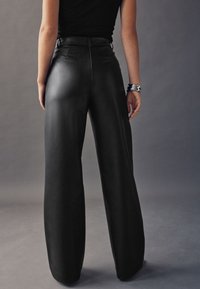 Zwarte leren broek met hoge taille en wijd uitlopende pijpen, met een gladde textuur en minimale stikdetails, gezien vanaf de achterkant.