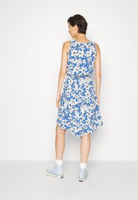 Vestido floral com um fundo azul e flores brancas e pretas, design sem mangas, cintura elástica e um comprimento justo ao joelho com barra assimétrica.