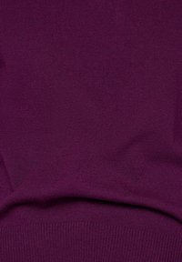 Lila Strickstoff mit glatter Textur und einem gerippten Saum. Das Material wirkt weich und leicht, ideal zum Übereinandertragen.