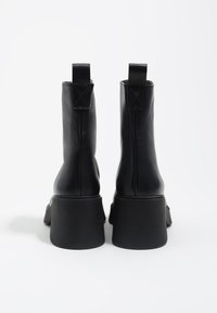 Botas de cuero negro hasta el tobillo con una suela de goma gruesa, tirador trasero y acabado suave. El diseño es elegante con bordes redondeados.