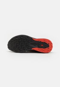 Sole di scarpa sportiva nera e rossa con un motivo robusto, caratterizzata da una presa testurizzata e tacchi pronunciati per la trazione.