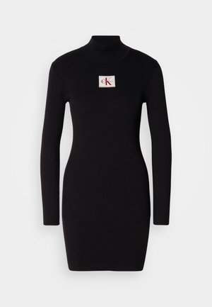 Abito lungo a maniche lunghe nero con collare alto e un'etichetta rettangolare del logo Calvin Klein sul davanti. Design semplice e aderente.