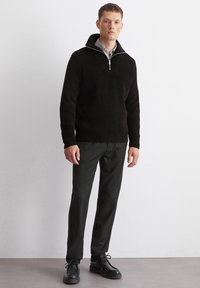 Black ribbed sweater with a zippered collar, paired with dark pinstriped trousers and black lace-up shoes, creating a structured look.