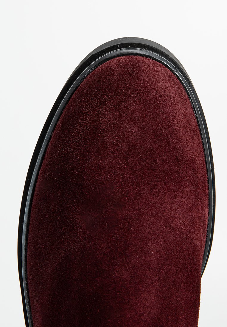 Bordeaux suède enkellaars met een gladde textuur, ronde neus en zwarte rubberen zool. Het bovenwerk heeft een subtiele glans en rijke kleurdiepte.