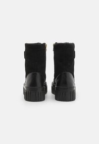 Botines negros hasta el tobillo con una parte superior de gamuza suave, suela de plataforma de goma y cierre de cremallera. Cuenta con un forro acogedor y un sutil logotipo en el talón.