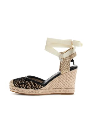 Beżowy pleciony sandał na koturnie z czarną siateczką na palcach, wstążkami do wiązania wokół kostki oraz teksturowaną podeszwą z liny.