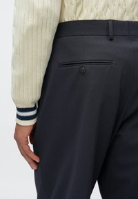 Ναυτικά παν trousers με πίσω τσέπη και κουμπί κλεισίματος. Φοριέται με ένα κρεμ πουλόβερ πλεκτό με μπλε ρίγες στους καρπούς.