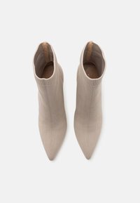Bottines beige en maille tricotée avec un bout pointu et une tige côtelée, dotées d'une doublure intérieure lisse et sans quincaillerie visible.