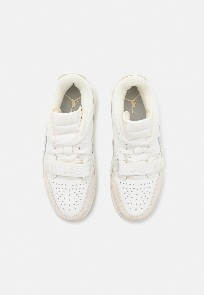 Zapatillas blancas con puntera perforada, acentos en beige texturizados, cuello acolchado y una correa con el logo "Nike". Logo dorado en las plantillas grises.