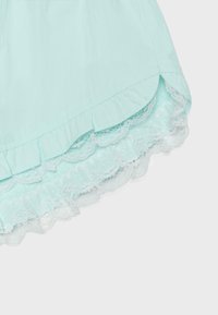 Tissu bleu clair avec ourlet froncé et bordure en dentelle blanche sur le bord, montrant une couture fine et une texture.