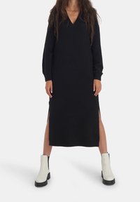 Svart stickad klänning med V-ringning, långa ärmar och sidoklipp, parat med krämfärgade ankelstövlar med svarta sulor.