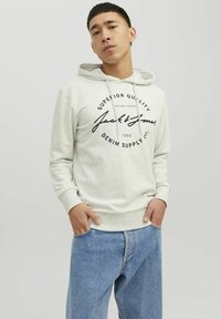 Lys grå hoodie med et stort sort logo, snoretræk i hætten og ribbede manchetter. Sammen med løstsiddende blå denim jeans.