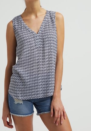 Mørkeblå og hvid mønstret ærmeløs top med V-hals, parret med denim shorts med afskårede ben. Stoffet ser letvægtsagtigt ud med en glat tekstur.