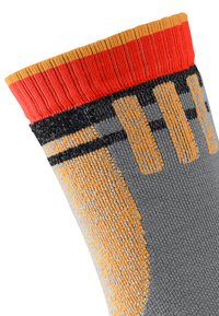 Chaussette en tricot grise avec des rayures diagonales orange et noires et un revers côtelé rouge. Le matériau semble texturé avec une surface globalement lisse.