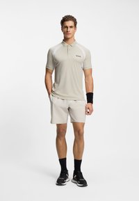 Light beige polo shirt with white accents and a small logo, paired with light shorts. Black athletic shoes and wristband complete the outfit.