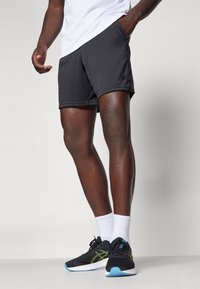 Svarta träningsshorts med elastisk midja, med en subtil logotyp vid fållen. Kombineras med svarta l öparskor och vita strumpor.