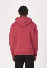 Felpa con cappuccio in rosa tenue con vestibilità comoda, polsini e orlo a coste. Tessuto morbido senza motivi o loghi visibili.