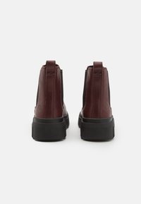 Burgunderfärgade läderankelboots med svarta elastiska sidopaneler och en tjock svart sula. Har logotypprägling vid hälen. Slät textur.