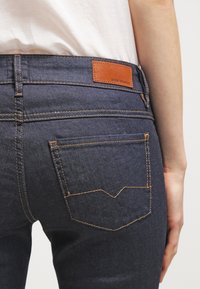 Los pantalones vaqueros de mezclilla azul oscuro presentan una etiqueta de cuero con la inscripción "BOSS ORANGE", con costuras en contraste en color naranja y un diseño de bolsillo único.