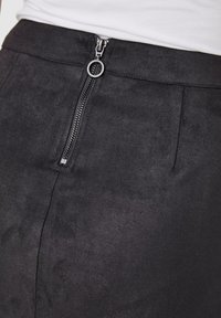 Svart nubuckkjol med en synlig dragkedja med en rund draghandtag, samt rena linjer med framfåror för extra designdetalj.