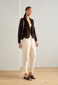 Svart kort blazer, beige crop top, texturerade krämfärgade byxor och svarta slidesandaler. Enkelt design med rak ben och dragsko.