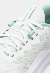 White athletic shoe featuring a textured mesh upper, light green accents near the laces, and a cushioned sole with a sleek design.
