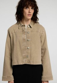 Beige denimjacka med krage, knappstängning och långa ärmar. Har en kortad design och subtil textur.