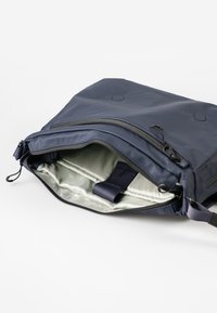 Marineblaue Tasche aus glattem, wasserdichtem Material; verfügt über ein offenes Fach mit einer hellen Innenfutter und einem Innengurt.
